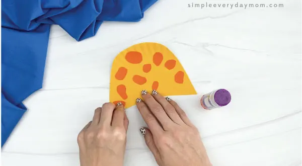 hands gluing spots to paper plate giraffe