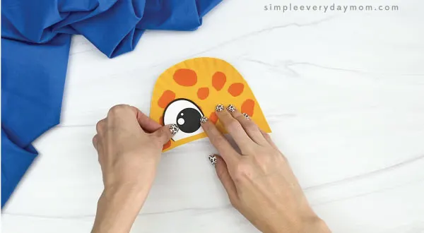 hands gluing eyes to paper plate giraffe