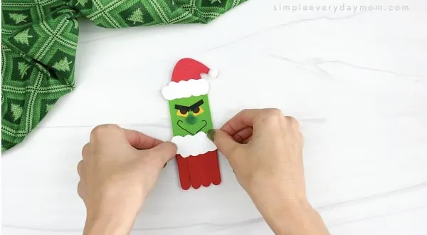 hands gluing santa suit fluff onto popsicle stick grinch craft