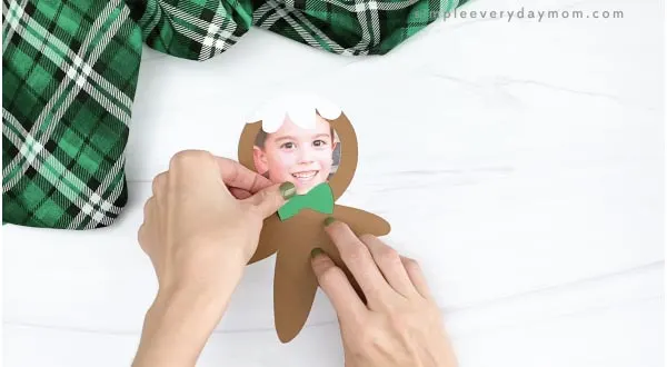 hand gluing bow photo to gingerbread man craft