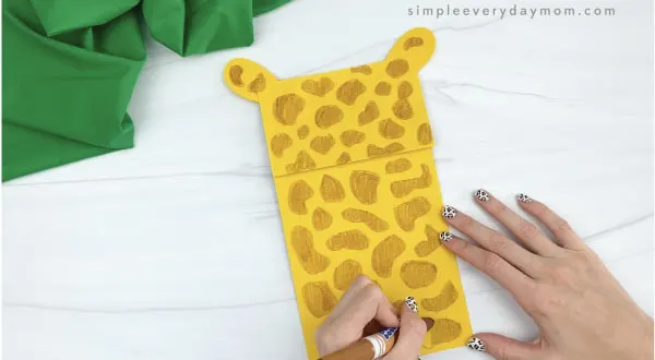 hands drawing spots on paper bag giraffe craft