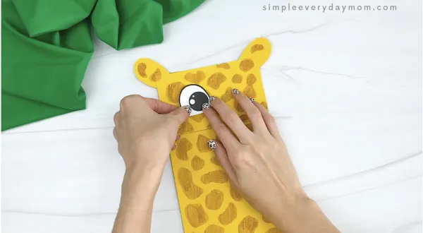 hands gluing eyes to paper bag giraffe craft