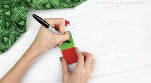 hands drawing mouth onto popsicle stick grinch craft