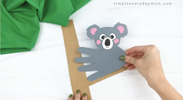 hand gluing handprint koala craft to paper tree