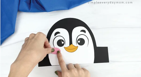 hands gluing cheeks onto penguin headband craft