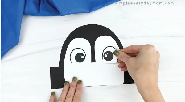 hands gluing eyes onto penguin headband craft