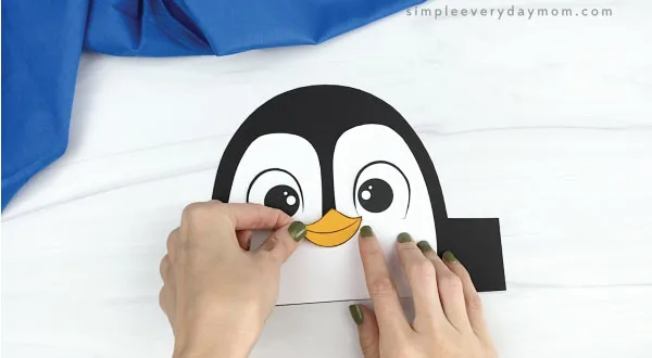 hands gluing beak onto penguin headband craft