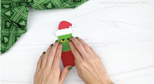hands gluing eyes onto popsicle stick grinch craft