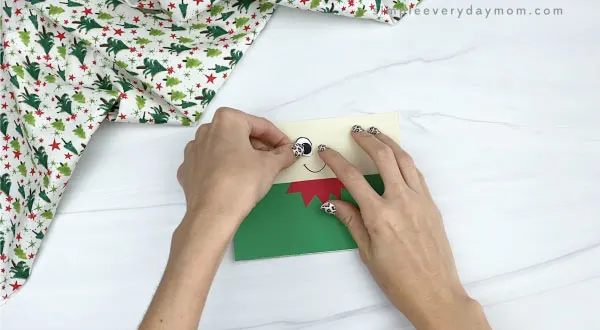 hands gluing eyes to elf toilet paper roll craft