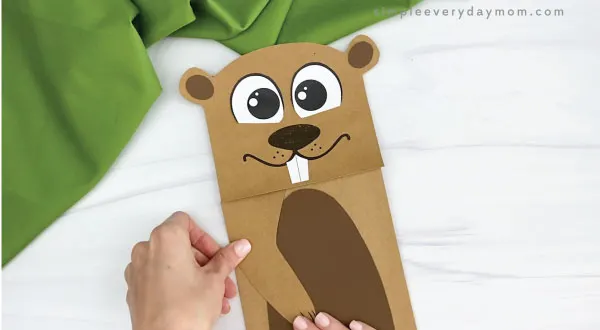hands gluing arms to paper bag groundhog craft
