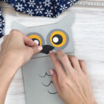 hands gluing beak to paper bag owl craft