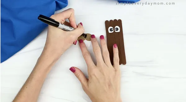 hands drawing nose onto popsicle stick walrus craft