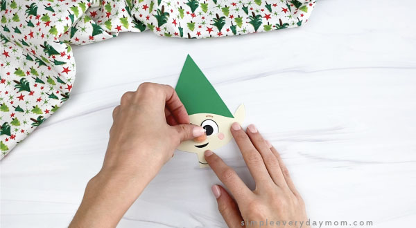 hands gluing pom pom nose to paper elf craft