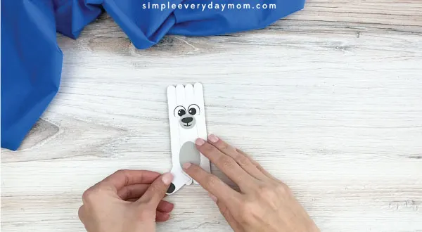 hands gluing outer legs onto popsicle stick polar bear craft