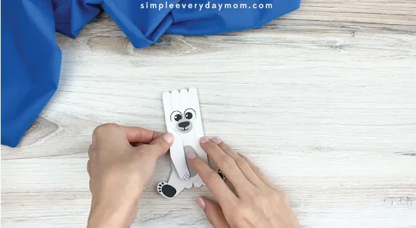 hands gluing inner legs onto popsicle stick polar bear craft