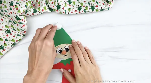 hands gluing pom pom to paper elf craft