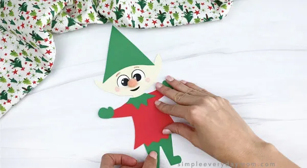 hands gluing pants onto paper elf craft