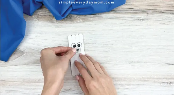 hands gluing mouth and nose onto popsicle stick polar bear craft