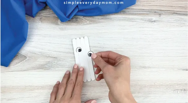 hands gluing eyes onto popsicle stick polar bear craft