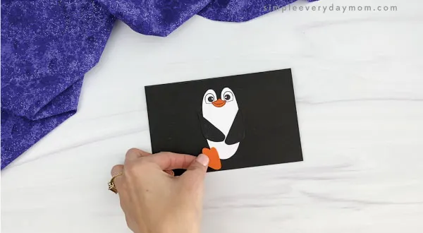 hands gluing feet to toilet paper roll penguin craft