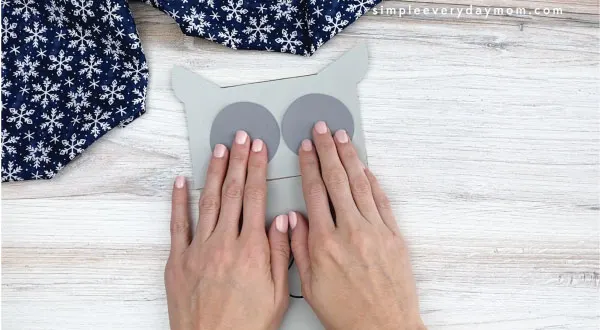 hands gluing gray circles to paper bag owl craft