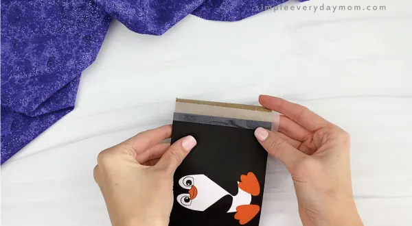 hands taping paper penguin to toilet paper roll