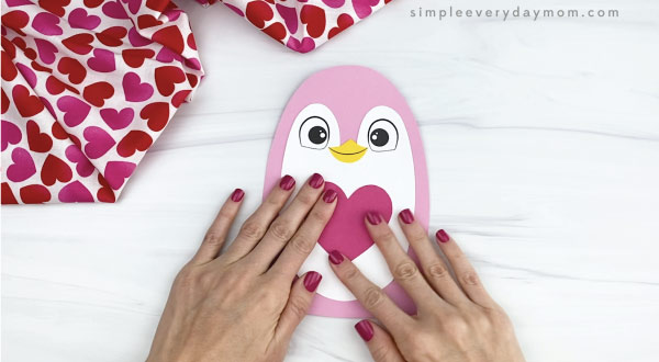 hand gluing heart onto penguin valentine craft