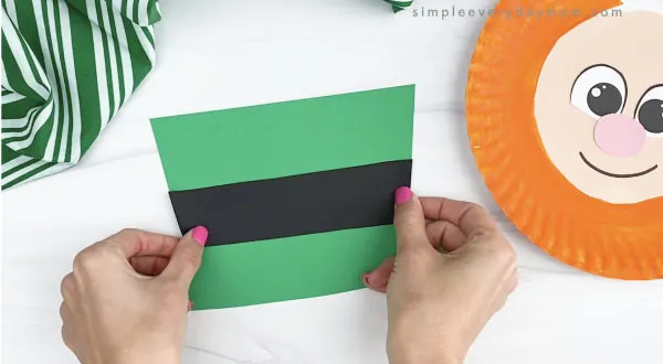 hand gluing black band to paper plate leprechaun hat craft