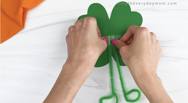 hand taping pipe cleaner legs to shamrock craft
