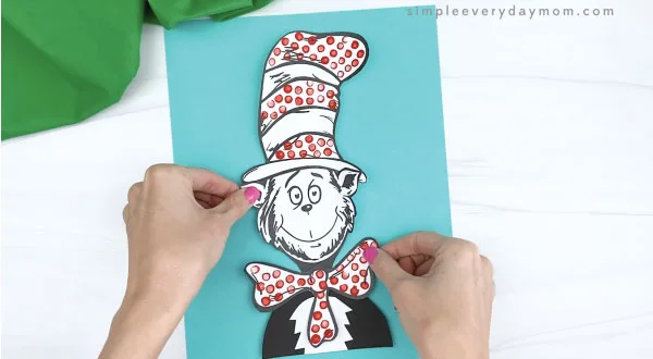 hands gluing cat in the hat craft to blue piece of paper