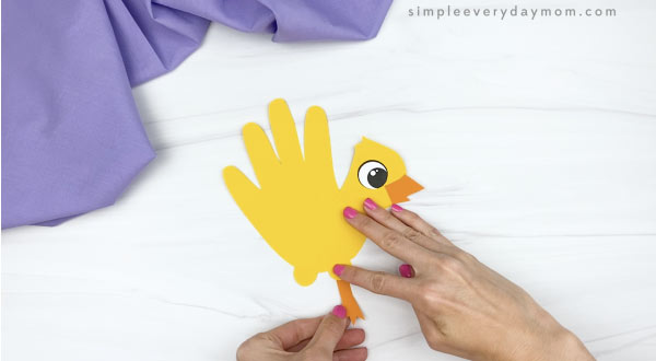 hand gluing leg to handprint chick