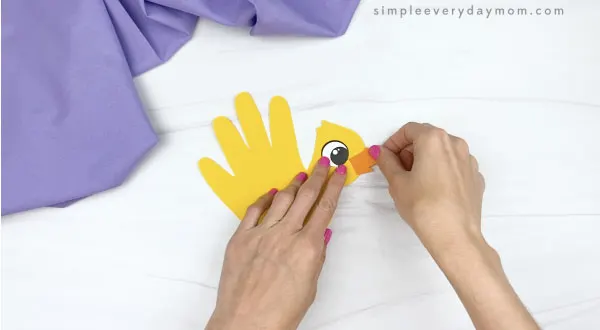 hand gluing beak to handprint chick