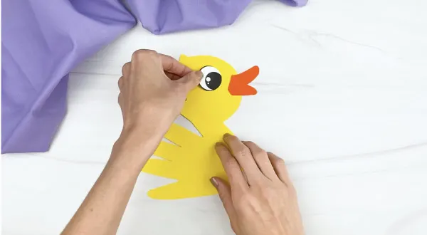 hands gluing eye to handprint duck craft