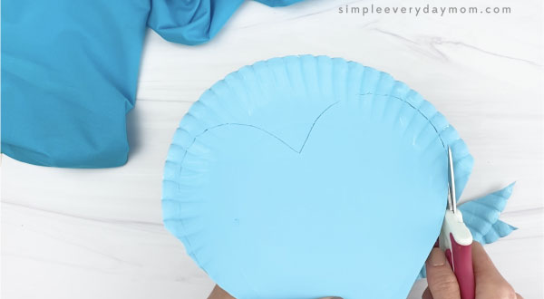 hand cutting out heart shape from blue paper plate