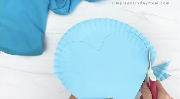 hand cutting out heart shape from blue paper plate