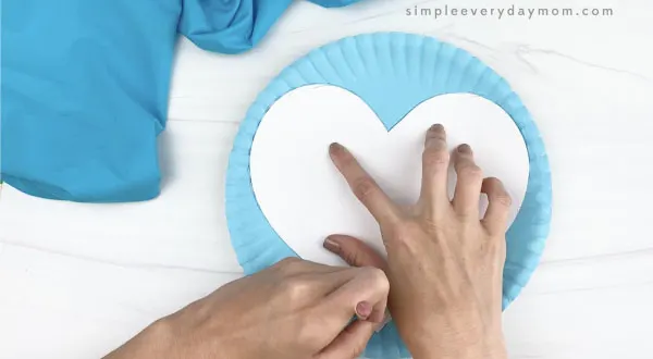 hand tracing heart template on blue paper plate