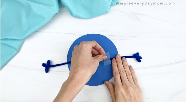 hand taping pipe cleaner arm to paper Earth craft