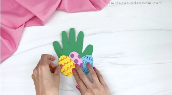 hand gluing paper Easter eggs to handprint Easter card craft