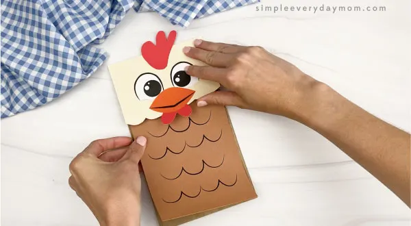 hand gluing body to paper bag chicken craft
