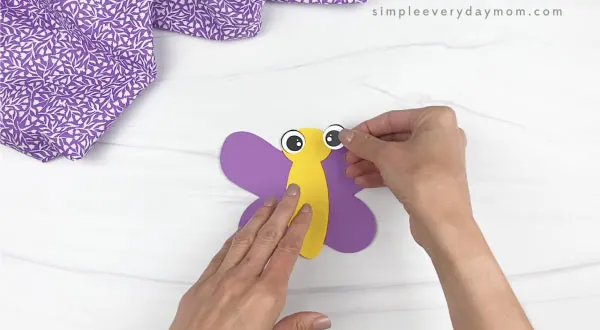 hand gluing eyes to butterfly stick puppet