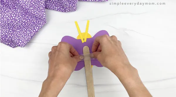 hand taping jumbo popsicle stick to butterfly puppet