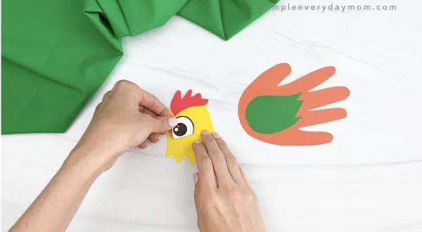 hands gluing eye to handprint rooster craft