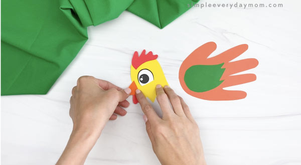hands gluing beak to handprint rooster craft