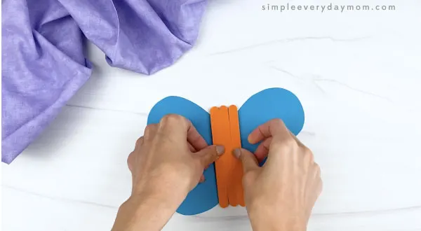 hand gluing popsicle stick body to popsicle stick butterfly craft