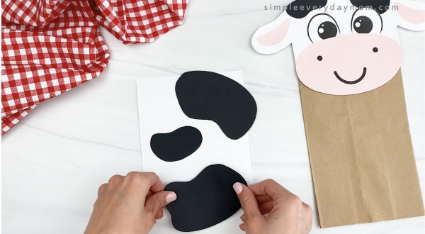 hand gluing spots to paper bag cow craft