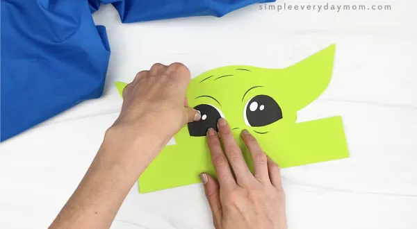 hands gluing eyes to Baby Yoda headband craft
