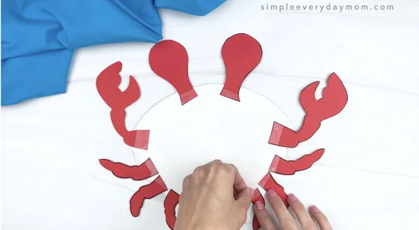 hand taping legs onto paper plate crab