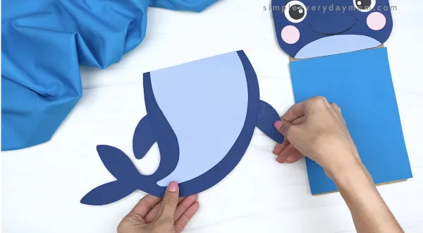 hands gluing fin to paper bag whale craft