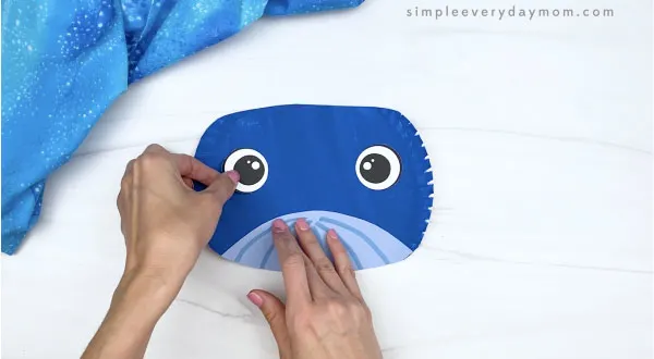 hand gluing eye onto paper plate whale craft