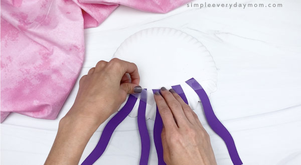 hand taping tentacles to paper plate jellyfish